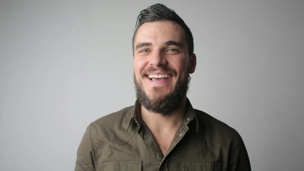 A imagem mostra um homem branco com cabelo curto e escuro e barba cheia. Ele usa uma blusa social verde escura. O homem aparece em primeiro plano, sorrindo, pois ele é um Bolsista CNPq que não concluiu doutorado e conseguiu o arquivamento do seu processo. O fundo é liso e claro.