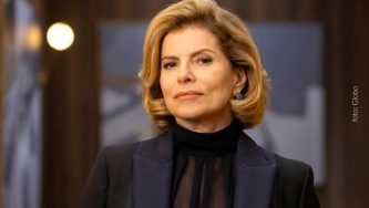 A imagem mostra uma mulher branca de cabelos curtos, castanhos e lisos até o ombro. Ela está em uma sala fechada e usa uma blusa preta e um paletó preto. Ela olha para a câmera com um olhar confiante. A mulher em questão é a atriz Debora Bloch, interpretando o papel de Odete Roitman, personagem da novela Vale Tudo, que tem feito o Brasil se perguntar de quem é a herança de Odete Roitman.