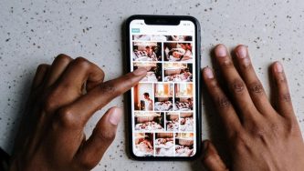 A imagem mostra um celular apoiado em uma mesa e duas mãos de uma pessoa negra mexem na galeria de imagens.